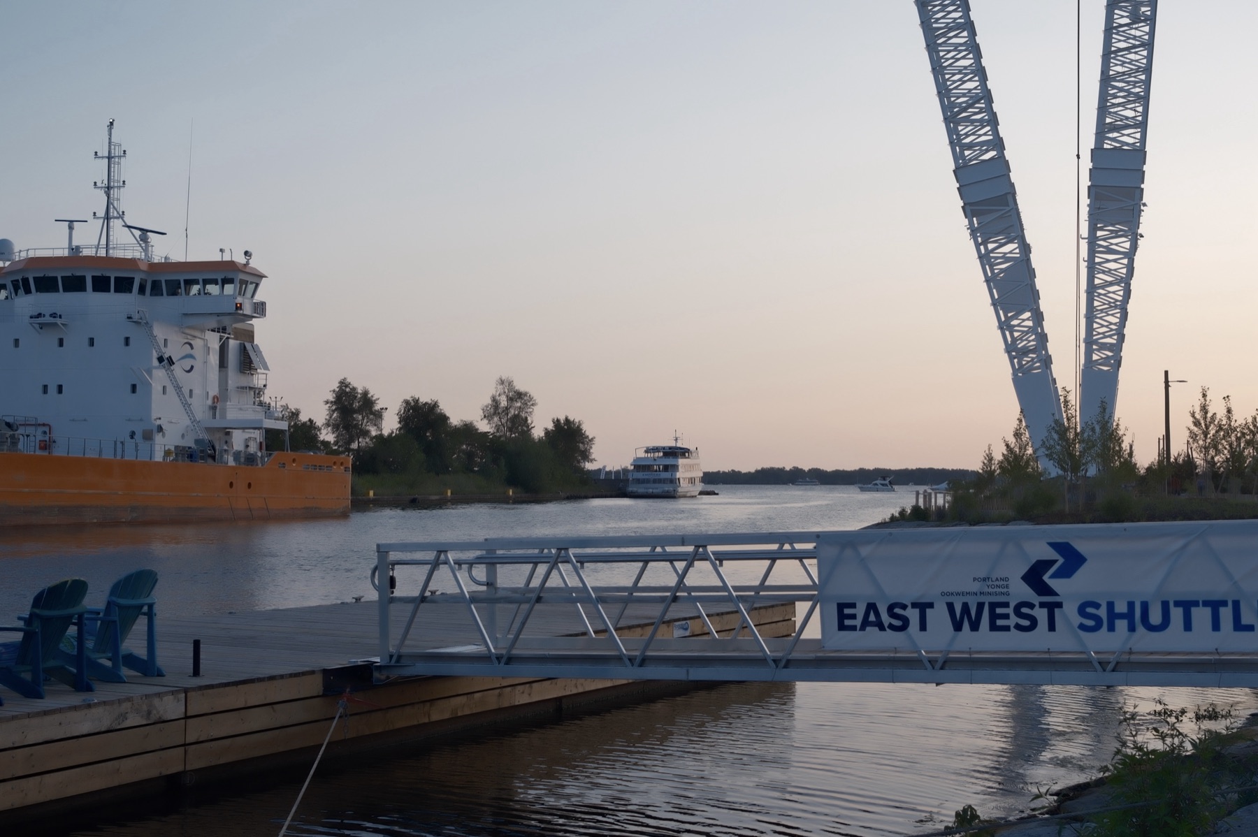 An orange ship, the white bridge arches and the East West Shuttle dock at dusk