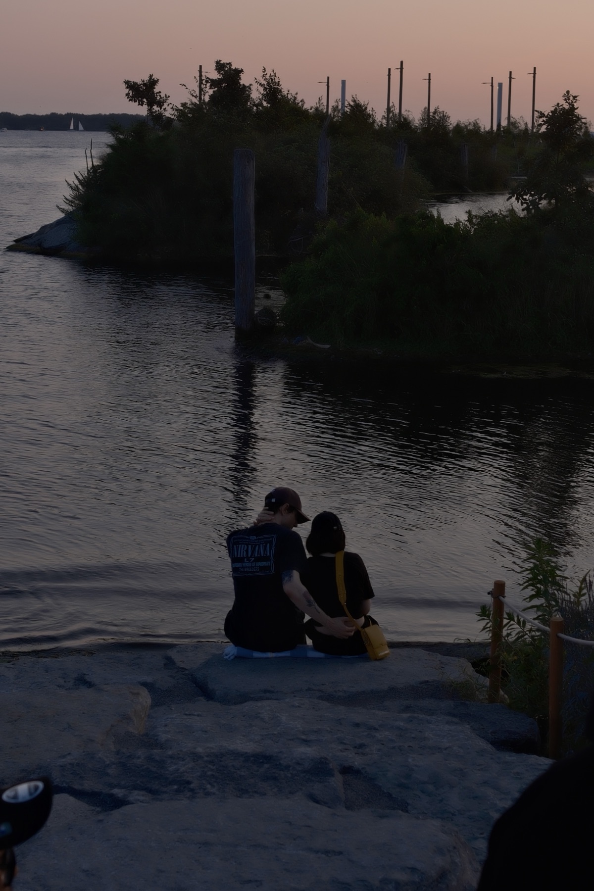 A couple sitting on the rocks at the water's edge, sunset on the lake