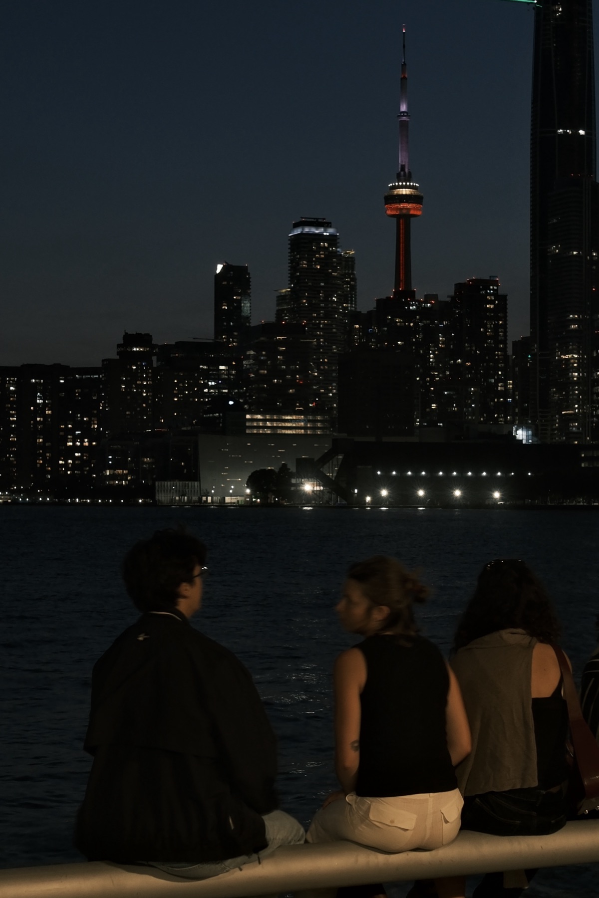 Three people on the railing, the CN Tower lit red