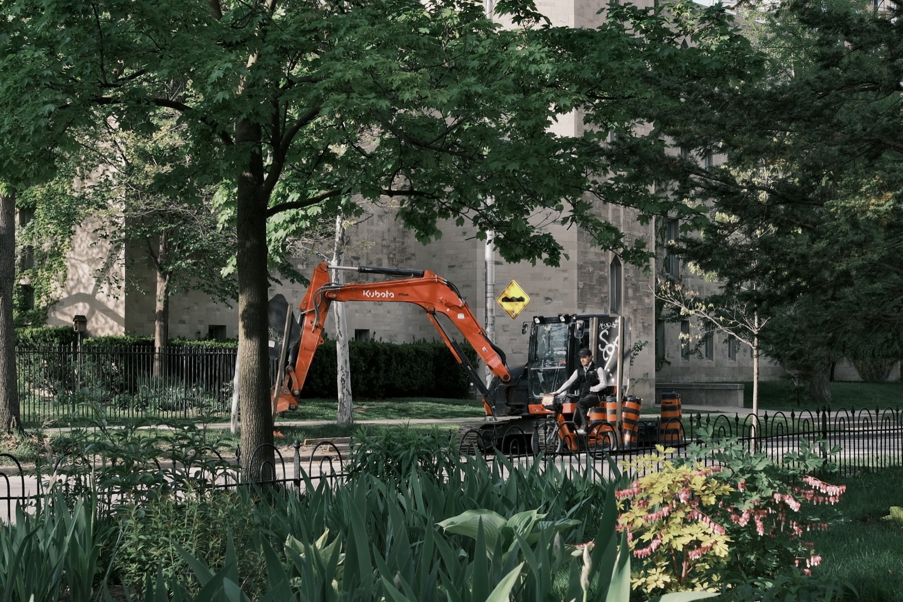 An orange excavator parked in a green parkette