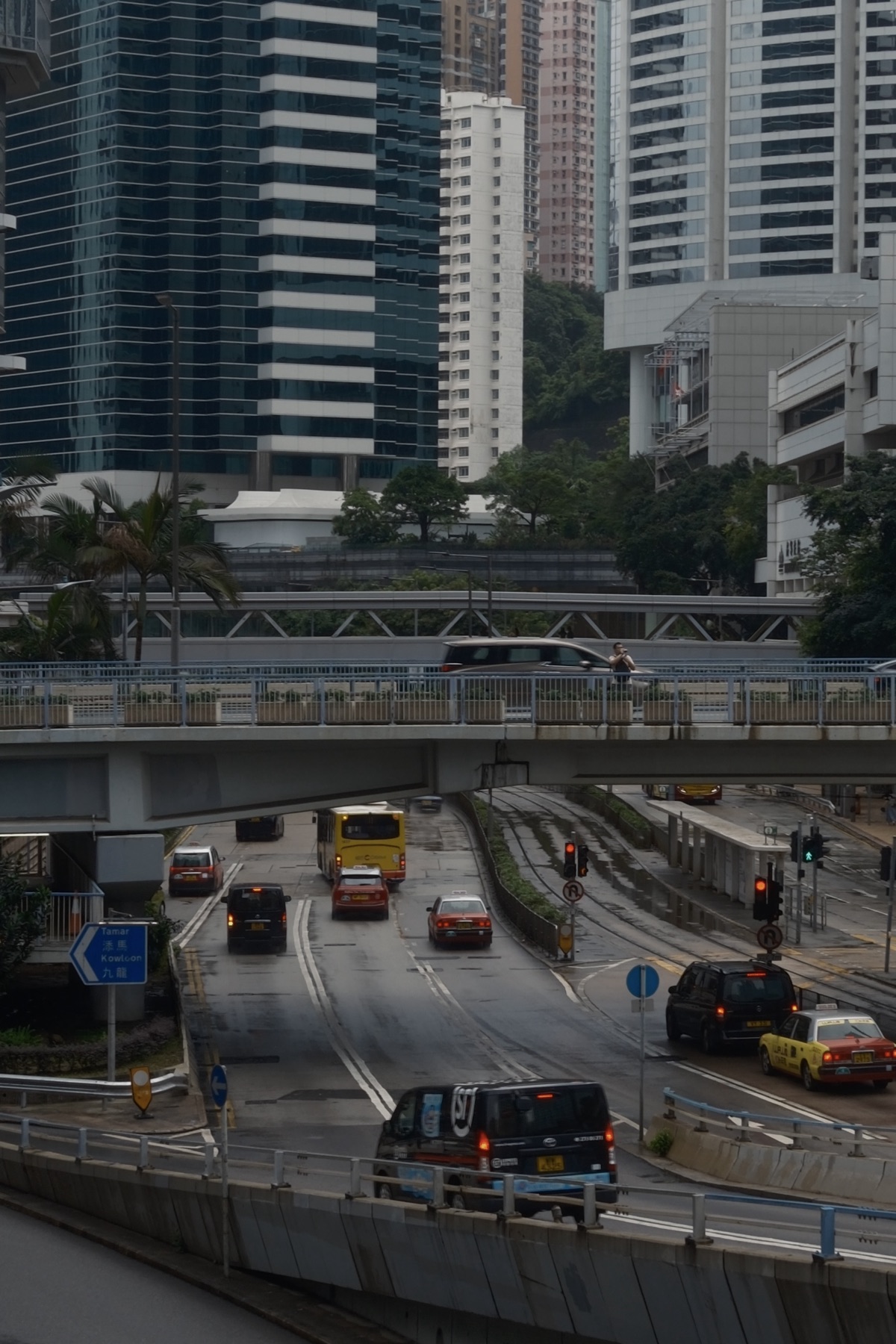 Wet roads under a footbridge, taxis and buses sorting into lanes