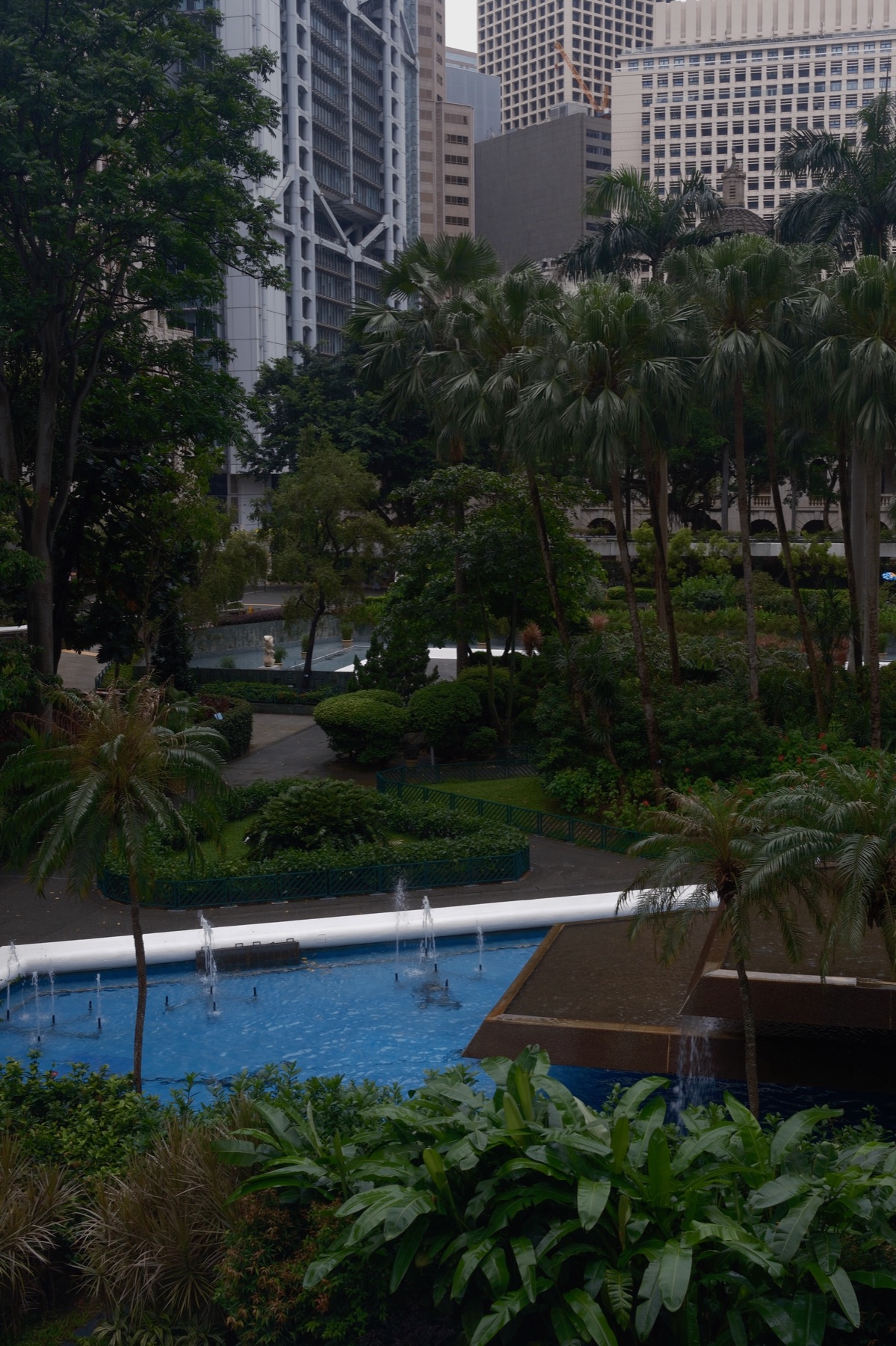 A blue fountain and palms below the bank towers