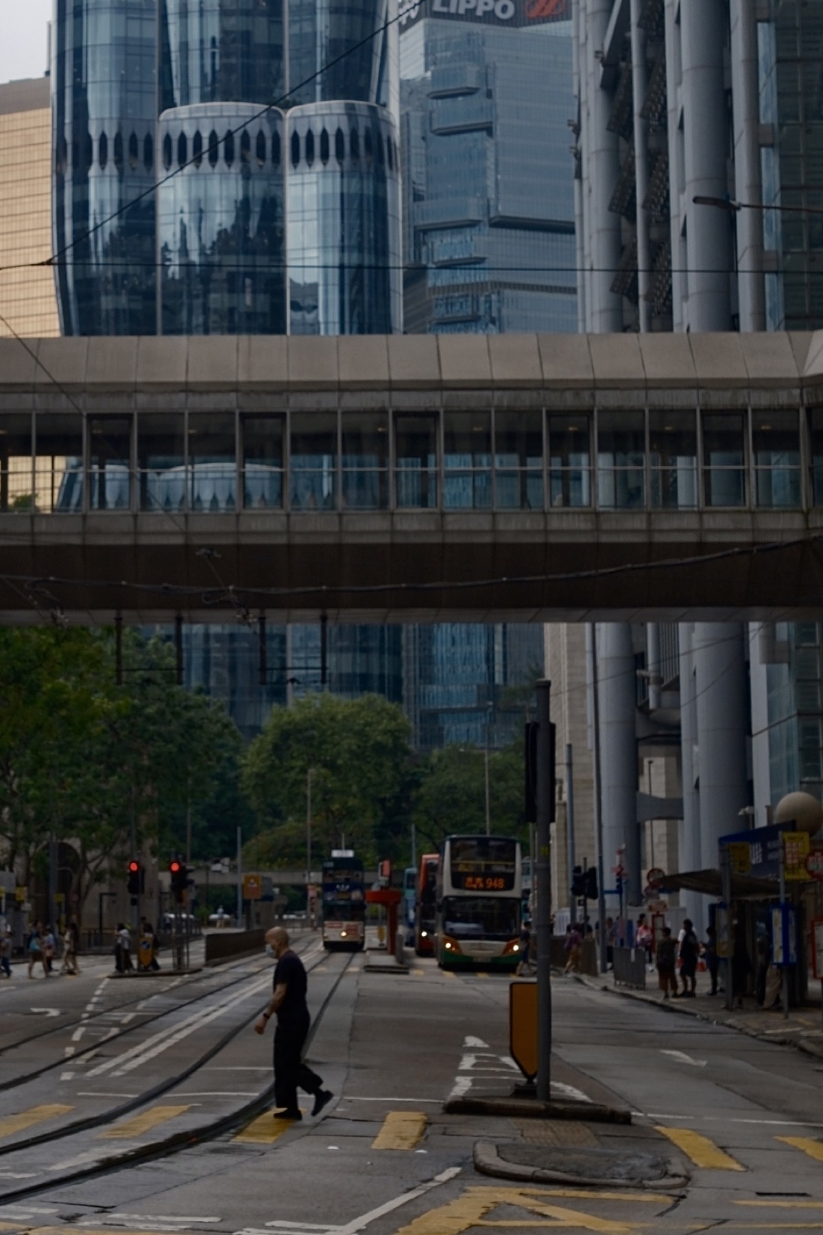 A man crossing the tram tracks under glass towers and a footbridge
