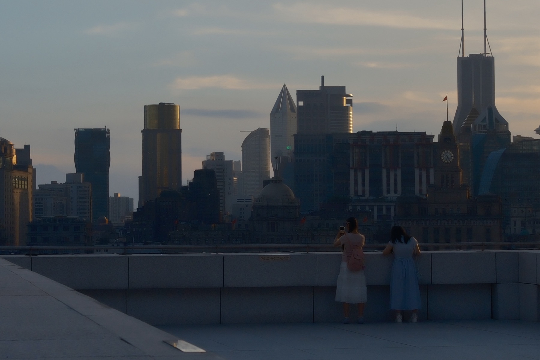 Two girls at the terrace rail photographing the Bund skyline at dusk