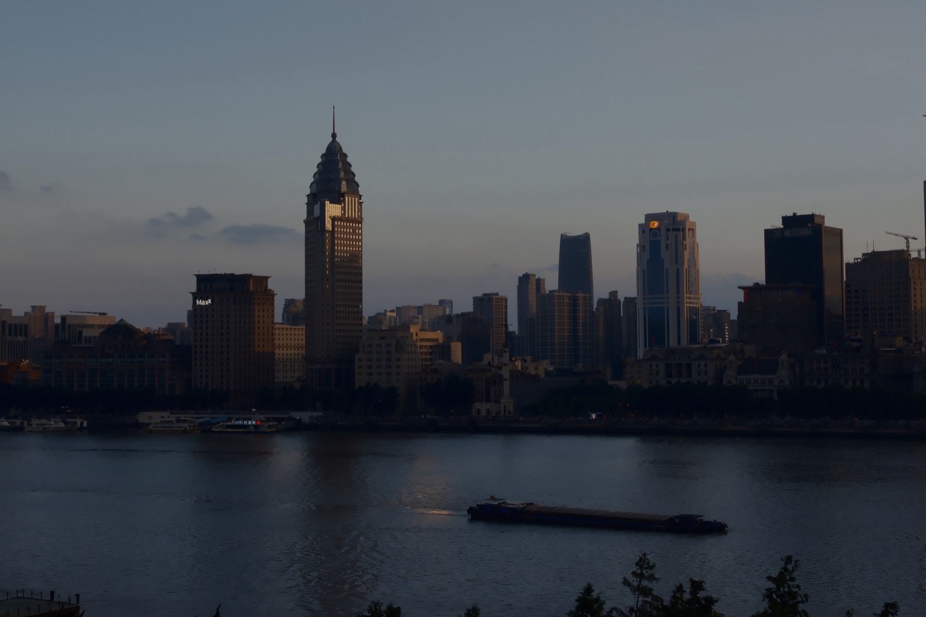 The old Bund towers catching the last sun, a barge crossing the river