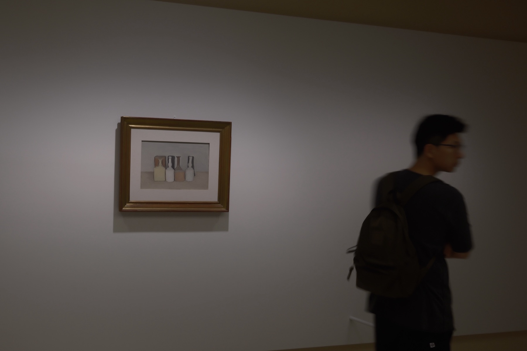 A Morandi still life in a gold frame, a visitor walking past in a blur