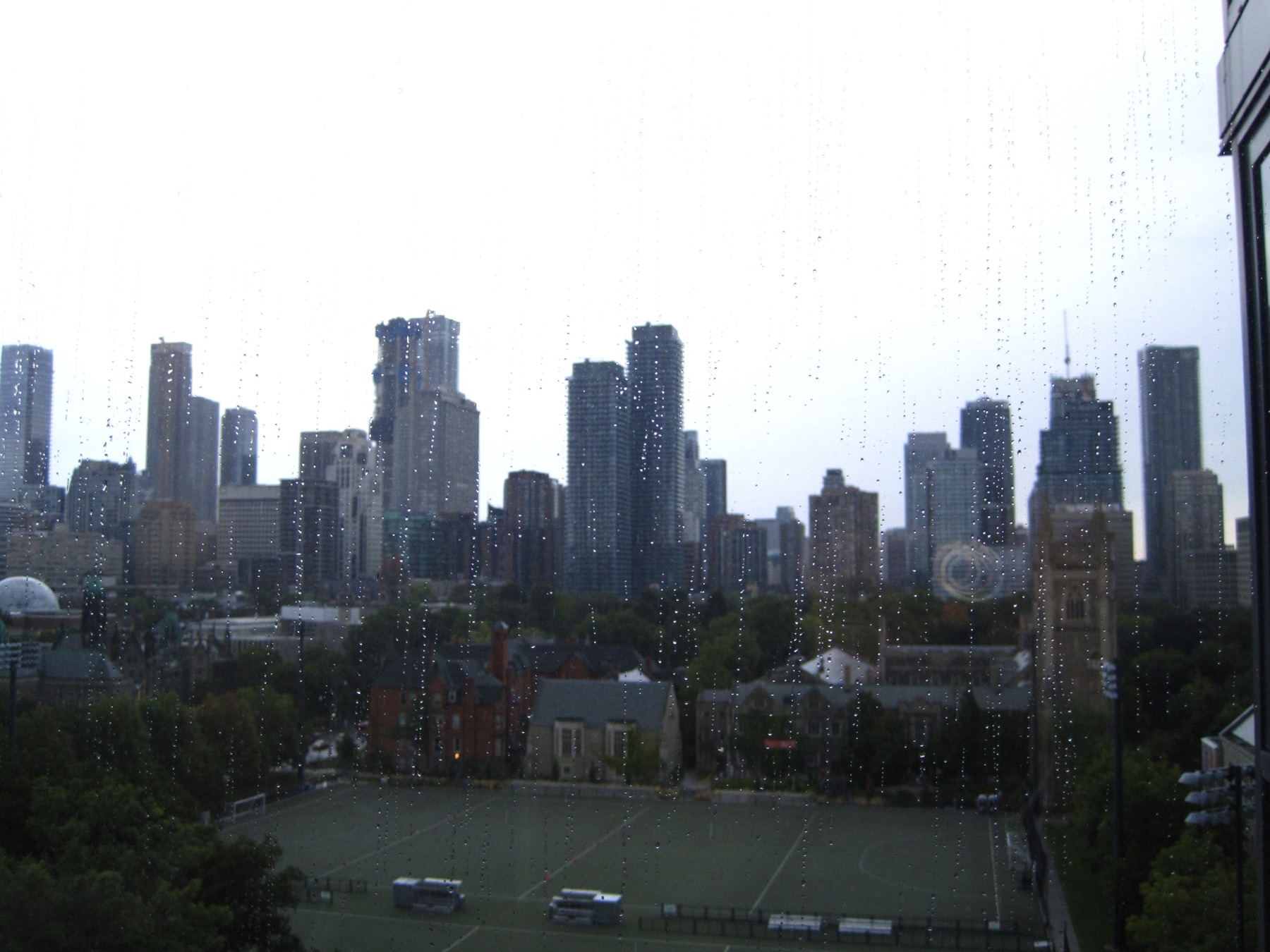 The Toronto skyline through a rain-flecked window over a green college field