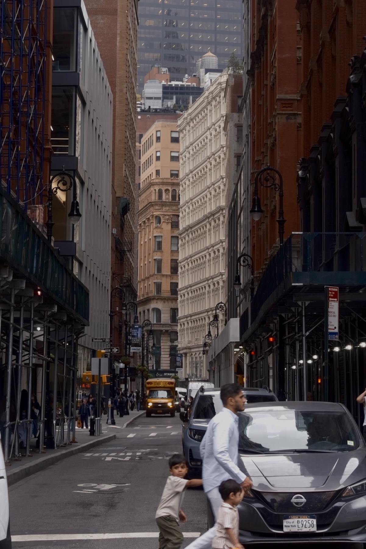 A street canyon in the Financial District, a man crossing with two children