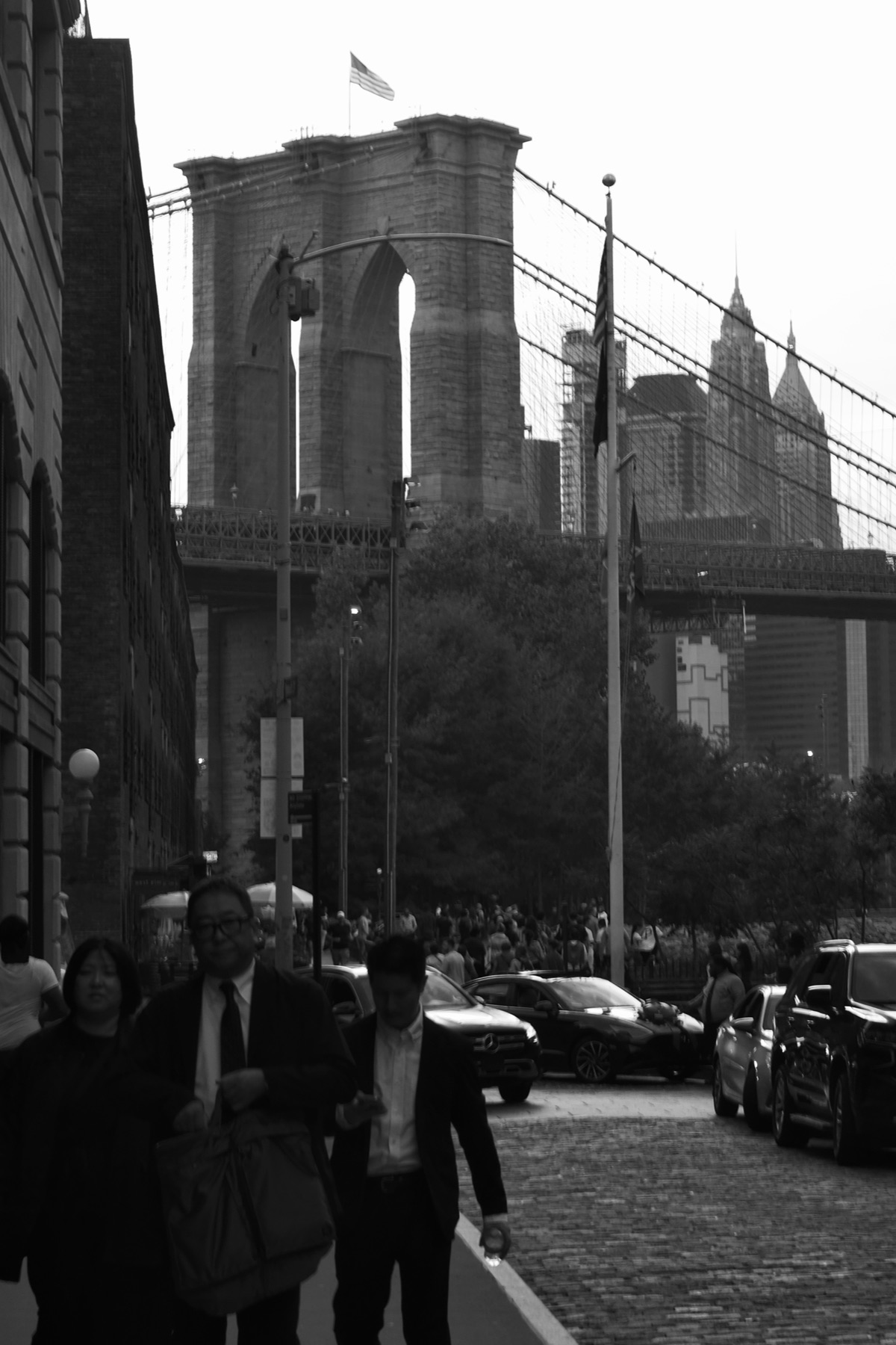 Brooklyn Bridge tower in black and white, people walking the cobblestones