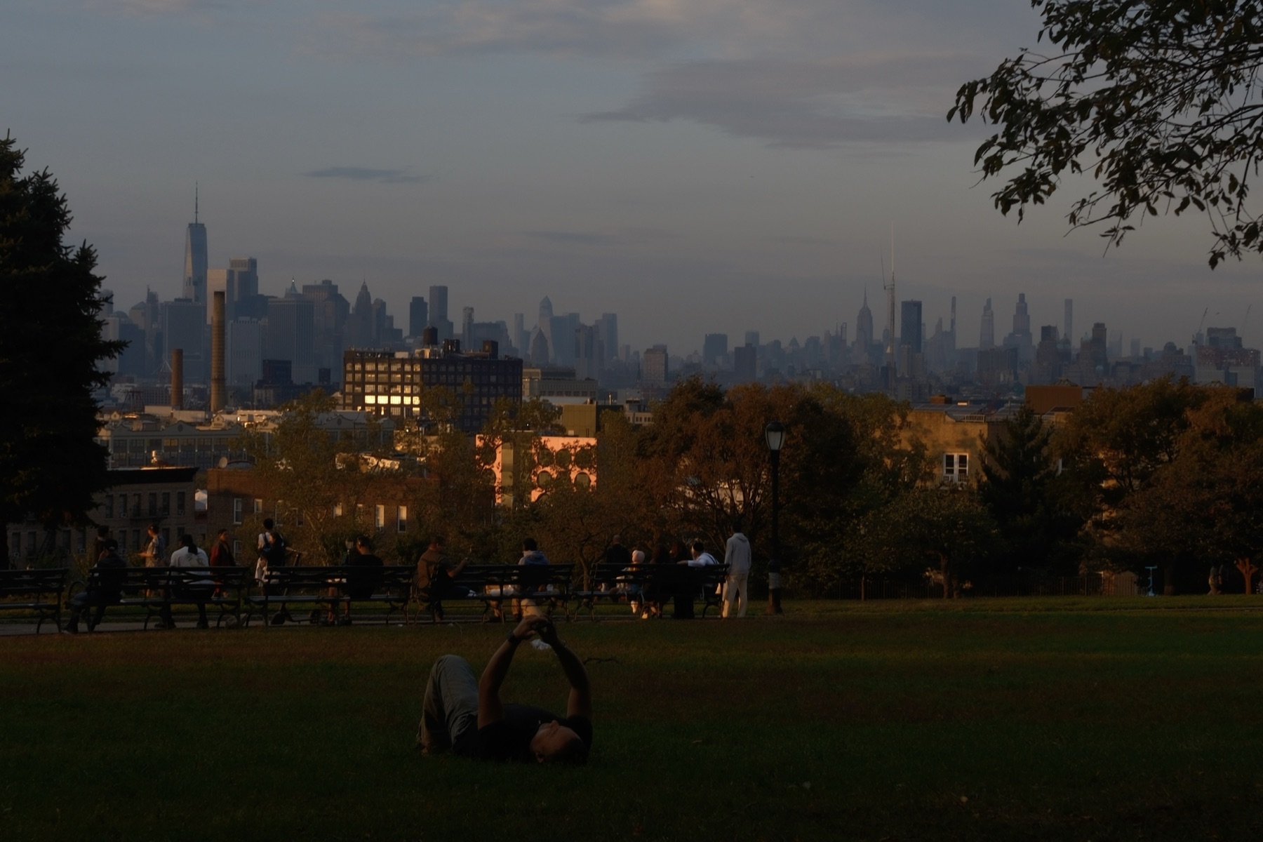A dusk lawn above the city, a man lying back to photograph the sky