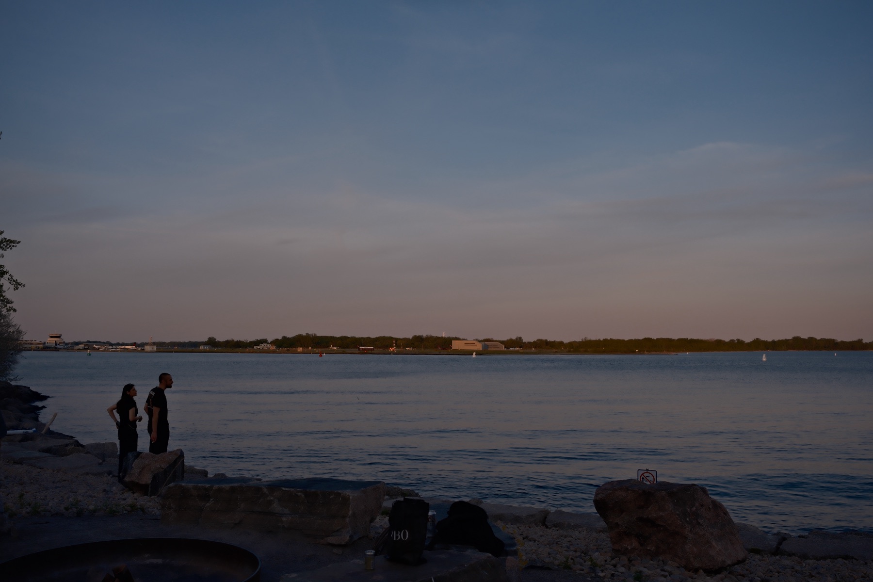 Two people on the breakwater, the far shore turning blue