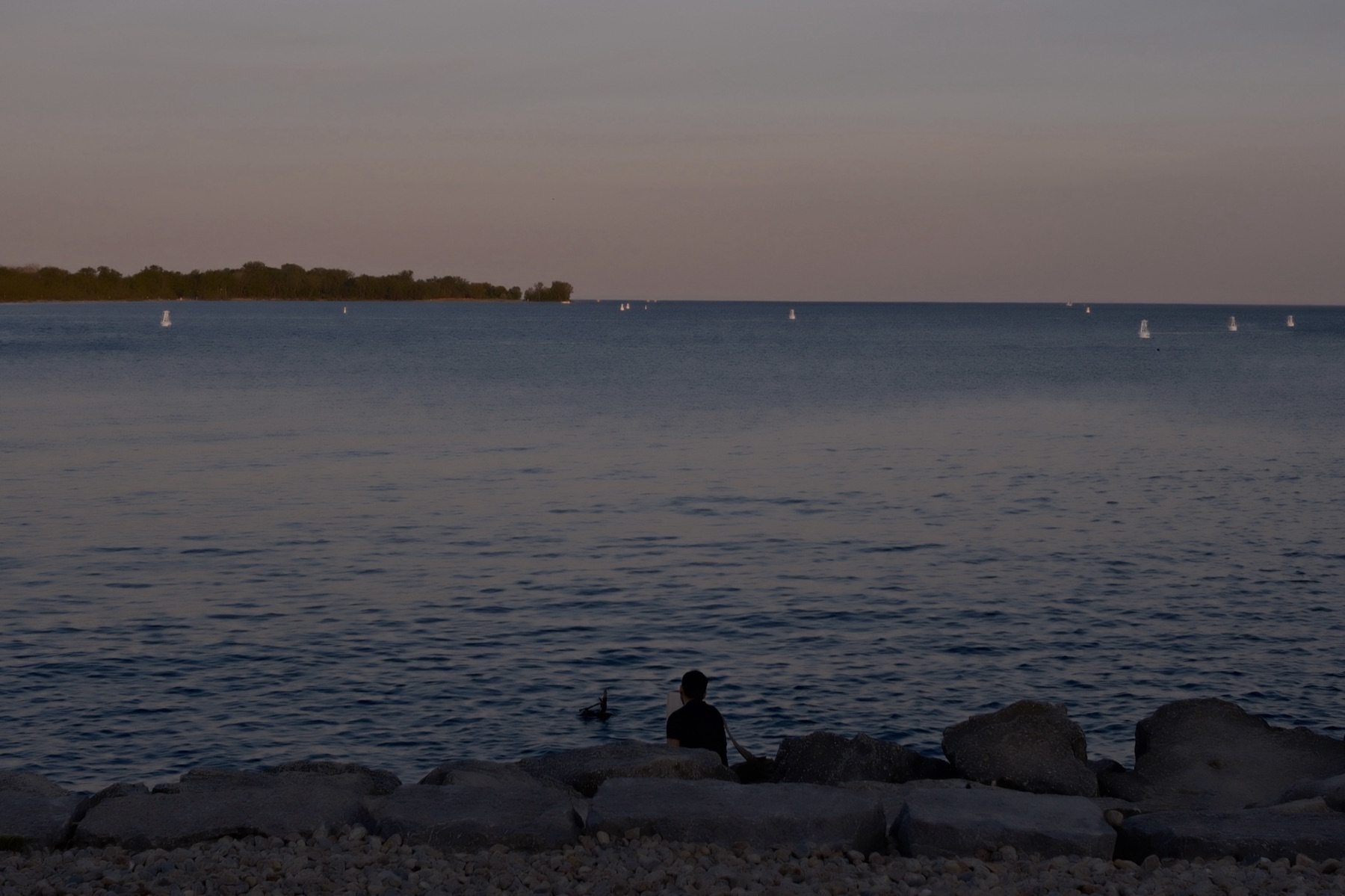 A lone figure at the waterline, sailboats out on the lake